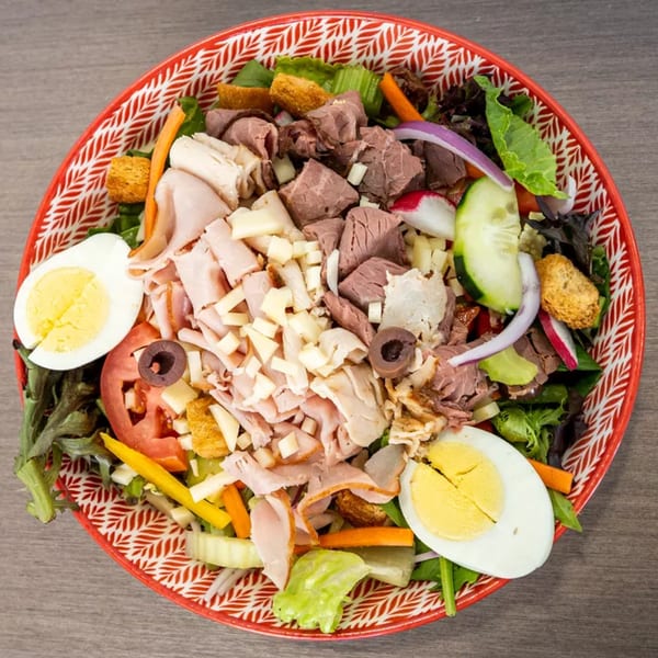 Overhead view of a chef salad with mixed greens, meats, cheeses, vegetables, and hard-boiled eggs.