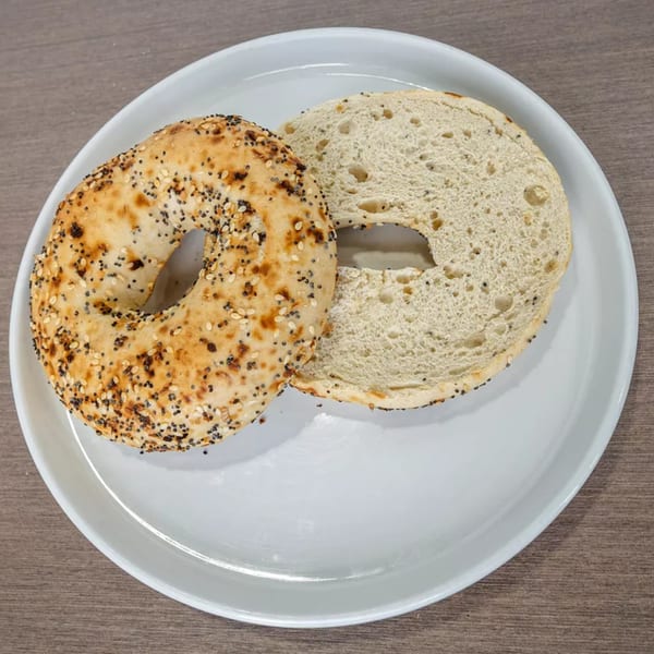 An everything bagel, sliced in half, rests on a white plate on a wooden table.