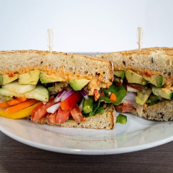 Two halves of a hearty sandwich filled with colorful vegetables, avocado, and a creamy sauce.