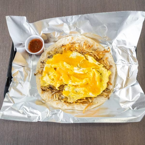 Breakfast taco with scrambled eggs, cheese, and hash browns, served with salsa in foil.